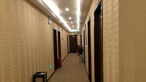 A hotel hallway with carpeted floors, doors on both sides, and a trash bin. - Nanjiang Shuangyu Holiday Hotel (Nanjiang)