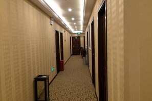 Pasillo de hotel con pisos alfombrados, puertas a ambos lados y un cesto de basura.