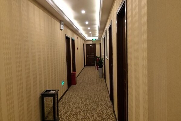 Corredor de hotel com piso coberto de carpete, portas em ambos os lados e uma lixeira.