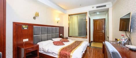A hotel room with a large bed, a bedside table, a desk, and a television.