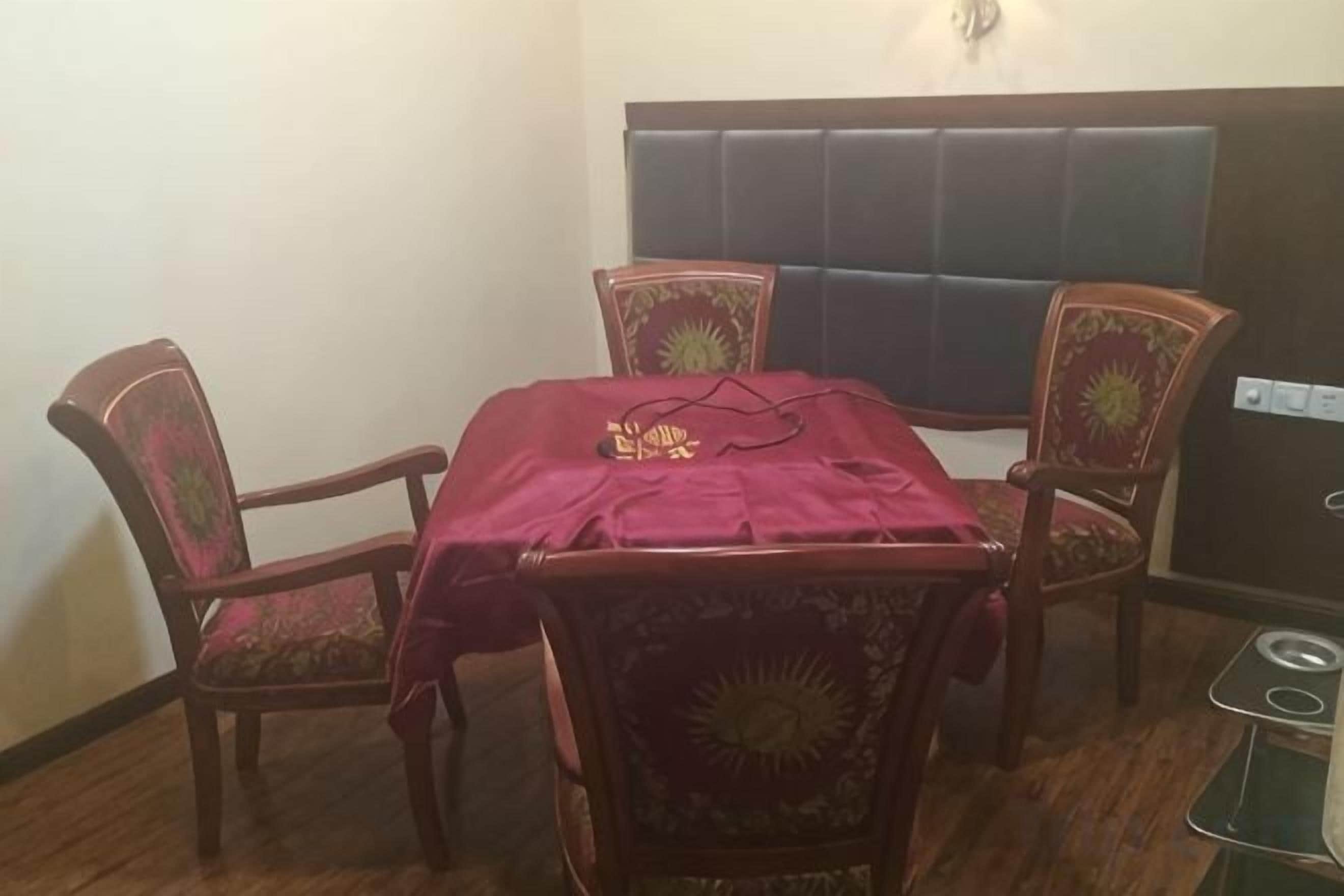 A dining area with a table covered by a red cloth, surrounded by four chairs with floral upholstery.