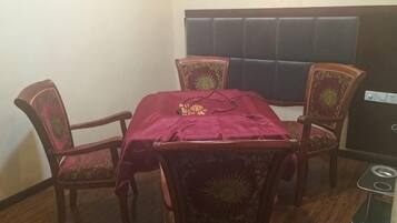 A dining area with a table covered by a red cloth, surrounded by four chairs with floral upholstery.