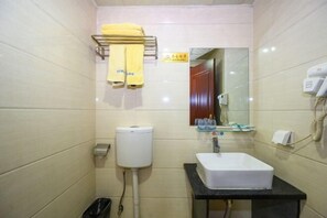Un baño con inodoro, lavamanos, espejo, toallero y un cubo de basura.