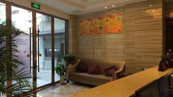 A reception area with a reception desk, a sofa, a potted plant, and a wall with informational posters.