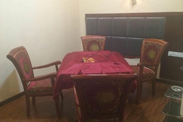 A dining area with a table covered in a red cloth, surrounded by four wooden chairs with floral upholstery. - Nanjiang Shuangyu Holiday Hotel (Nanjiang)