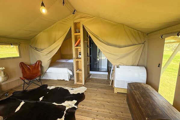 A tent with two beds, a wooden ladder, a bench, a cowhide rug, and a hanging light bulb.