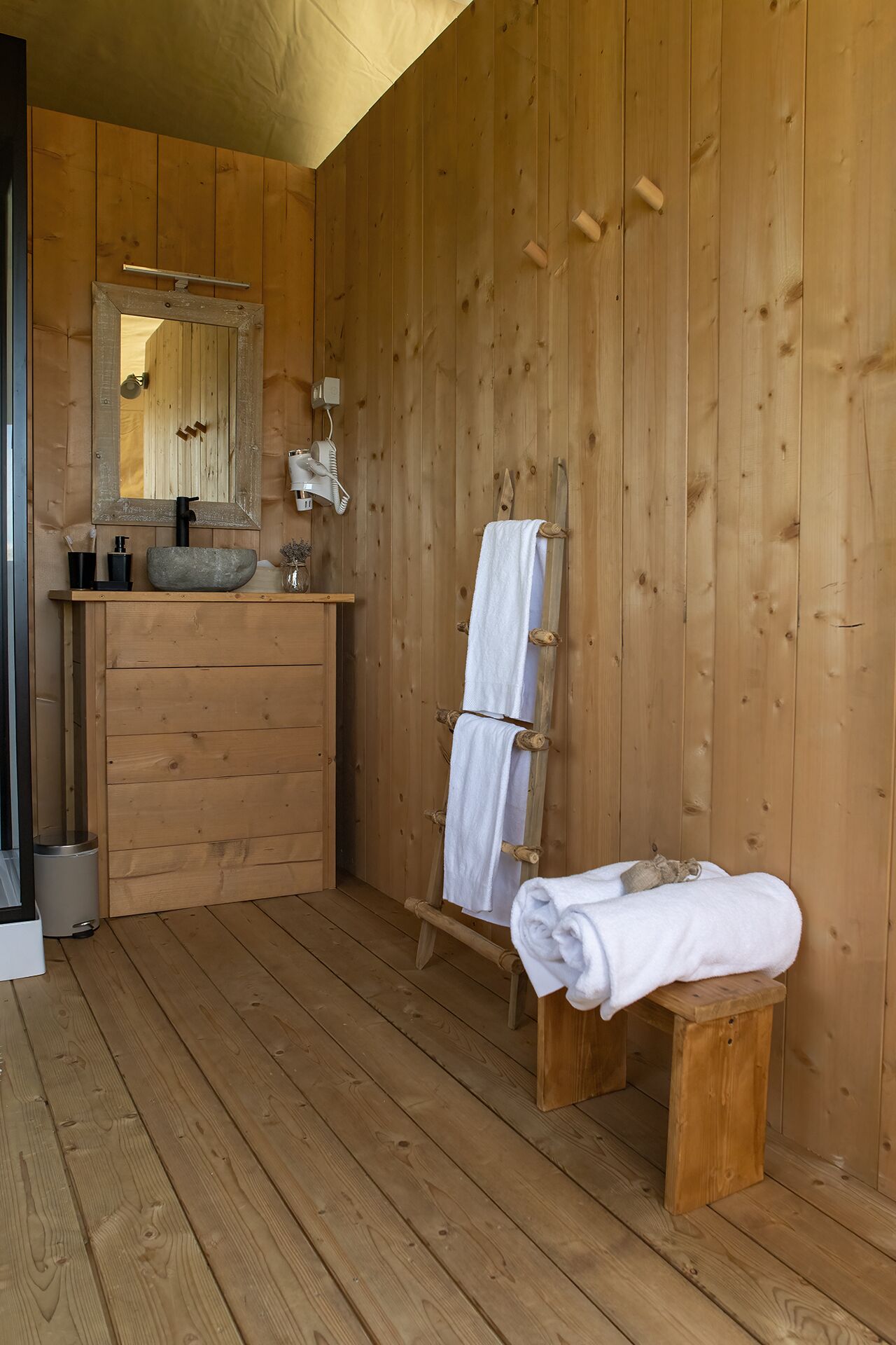 A wooden cabin bathroom with a wooden vanity, a large mirror, a towel rack, and a bench.