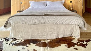 A bedroom with a wooden headboard, a bed with white bedding, two bedside tables with lamps, and a cowhide rug on the floor. - Tenuta San Lodovico (Scansano)