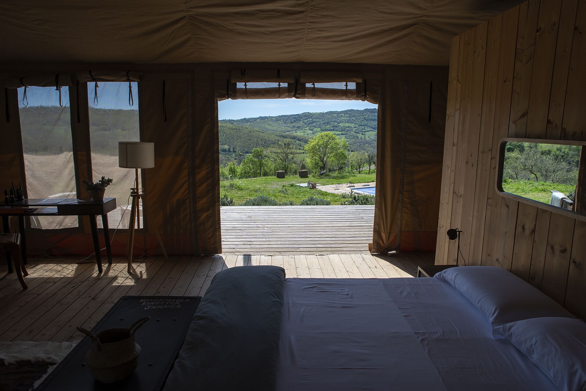 Une chambre avec un grand lit, un bureau et une vue sur un paysage verdoyant, visible à travers une porte ouverte.