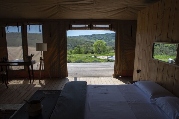 A bedroom with a large bed, a desk, and a view of a green landscape through an open door. - Tenuta San Lodovico (Scansano)