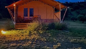 A single-story, A-frame tent with a porch and a small window, set in a grassy field with a dark blue sky. - Tenuta San Lodovico (Scansano)