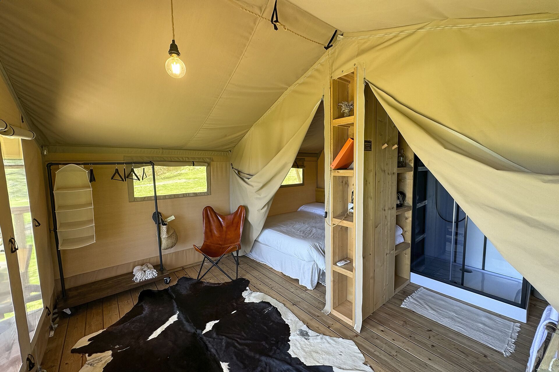 A tent with a bed, a chair, a shelf with items, and a cowhide rug.
