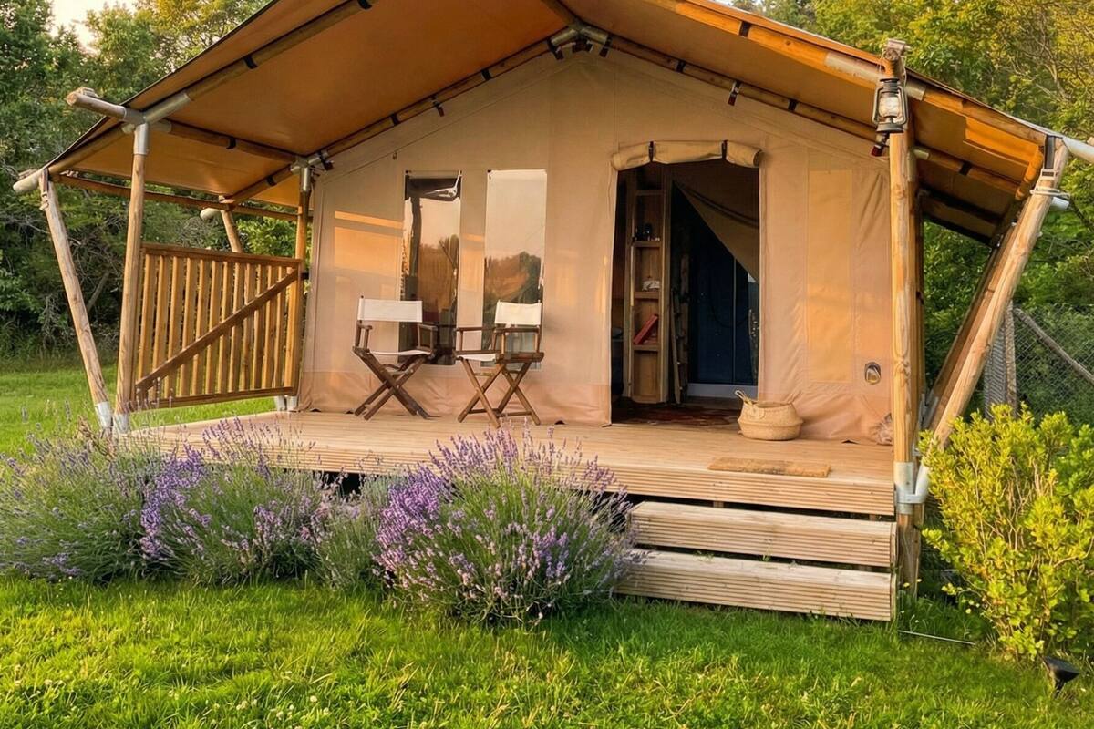 A tented accommodation with a covered porch, two folding chairs, and a door leading inside.