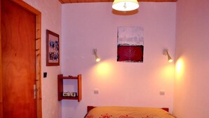 Een slaapkamer met een bed, een houten deur, een plank met spiegel en wandlampen.