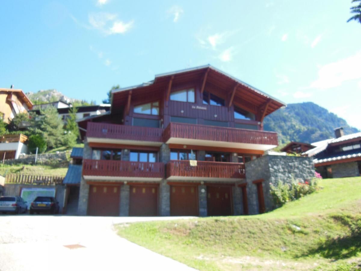 Un edificio a più piani con balconi, una facciata in pietra e uno sfondo montuoso.