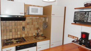 Een compacte keuken met een magnetron, kookplaat, spoelbak en koffiezetapparaat op het aanrecht.
