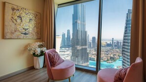 Una camera moderna con una grande finestra vista sulla città, due poltrone rosa, un quadro decorativo e un vaso con fiori.
