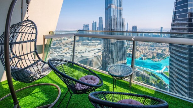 Un balcone con vista sulla città, tra cui un grattacielo, e tre poltrone in vimini con cuscini.