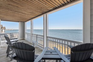 Um deck coberto com cadeiras Adirondack e uma mesa, com vista para a praia e o oceano.