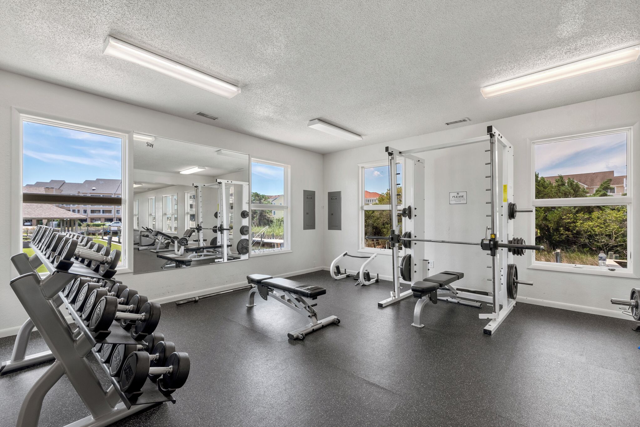 A gym with weightlifting equipment, mirrors, and large windows.