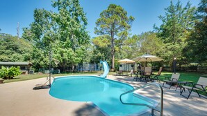 A swimming pool with a slide, surrounded by trees and outdoor seating. - Pet-Friendly Fort Valley Home w/ Private Pool (Fort Valley)