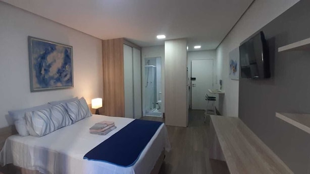 Habitación de hotel con cama, lámpara de noche, televisor montado en la pared y baño visible a través de una puerta abierta.