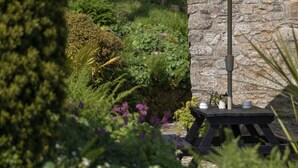A stone wall, a wooden table with a bench, and an umbrella. - A stunning Cornish barn, ideally located for visiting the North and South Coast. (Altarnun)