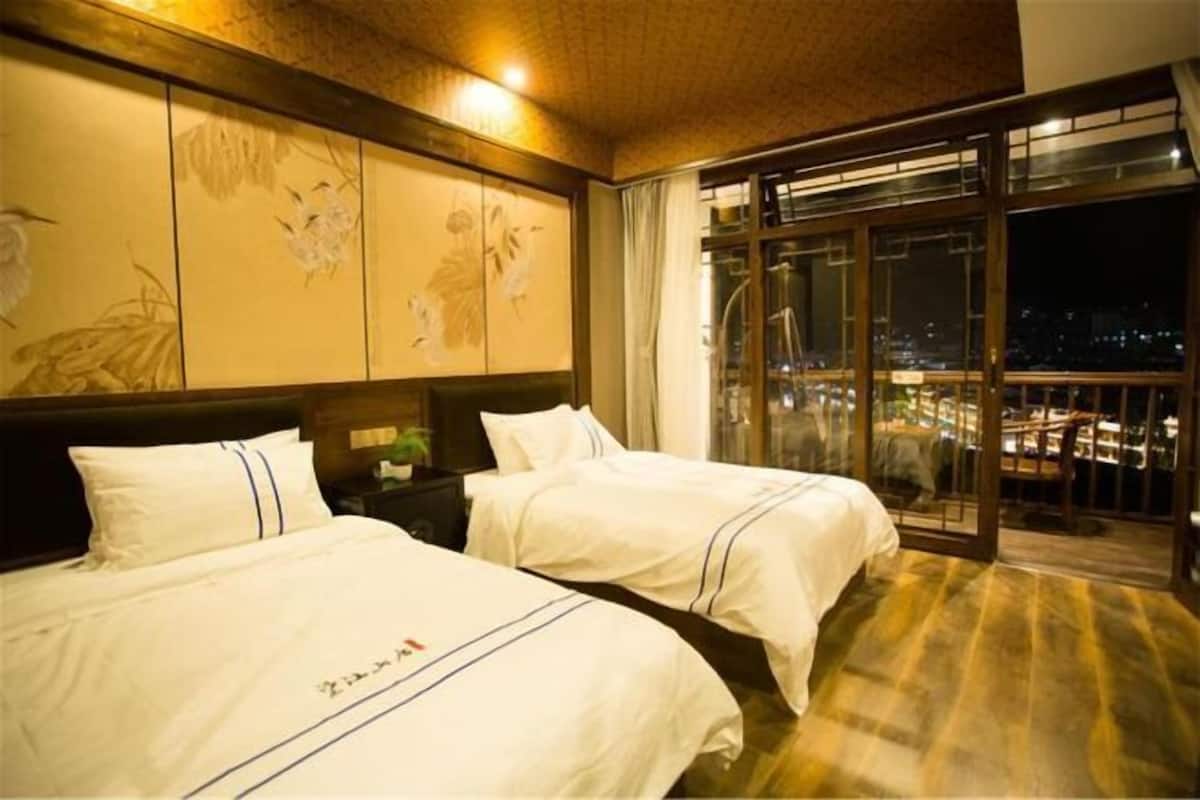 Une chambre d’hôtel avec deux lits, une grande fenêtre donnant sur la ville et des œuvres d’art traditionnelles accrochées au mur.