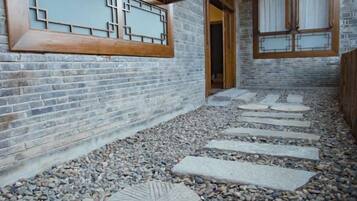 A courtyard with a stone pathway leading to a wooden door, surrounded by brick walls and a traditional window design.