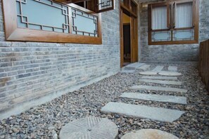 Ein Innenhof mit einem Steinweg, der zu einer Holztür führt, umgeben von Backsteinmauern und einem traditionellen Fensterdesign.