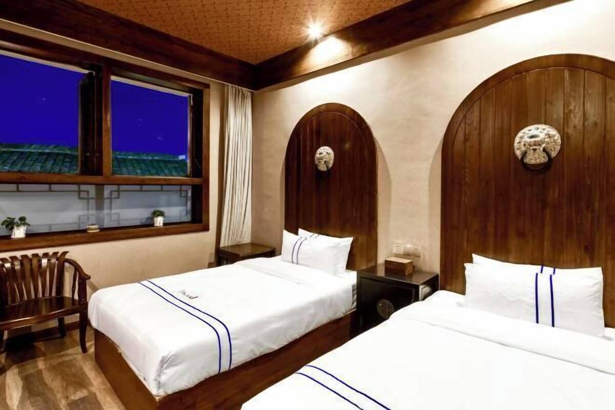 Une chambre d’hôtel avec deux lits, des têtes de lit en bois, une table de chevet, une chaise et une fenêtre donnant sur le toit.