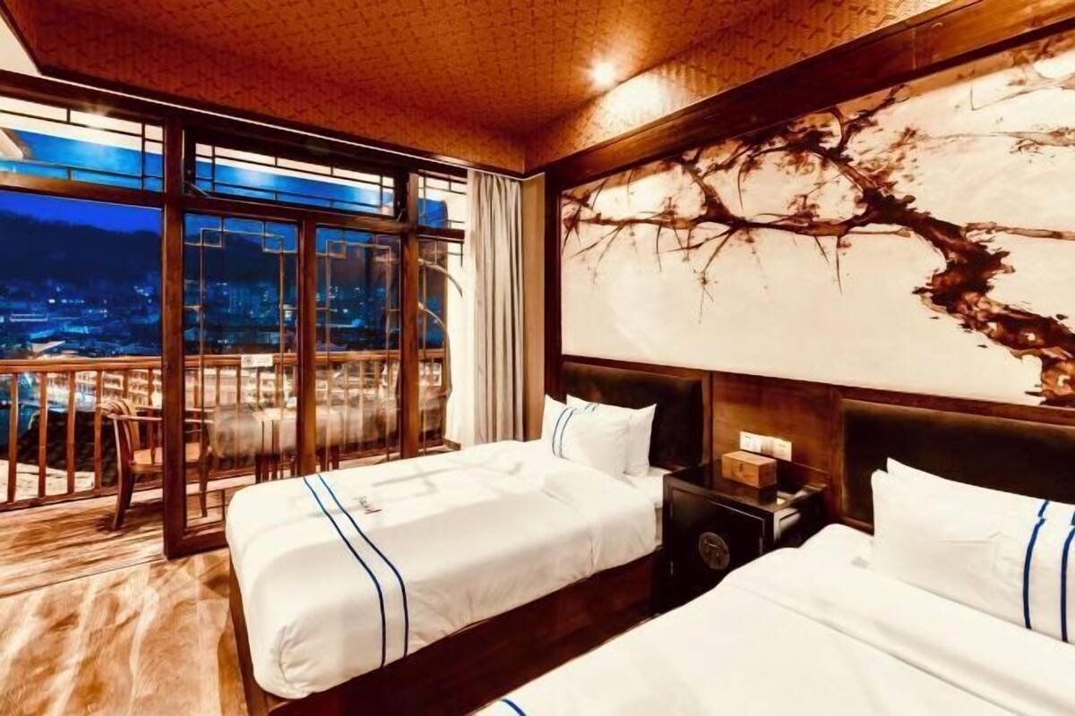 Une chambre d’hôtel avec deux lits, une grande fenêtre donnant sur un beau paysage et une peinture murale.