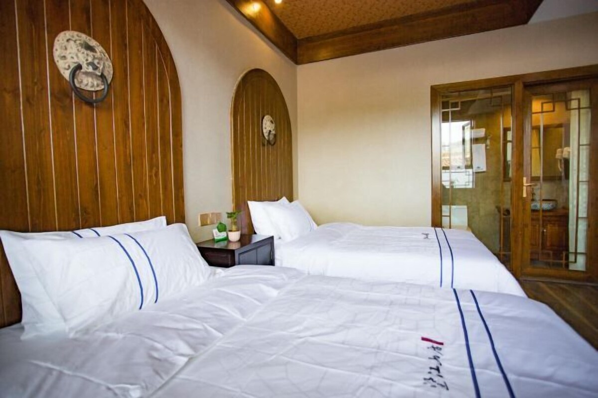 A hotel room with two beds, wooden paneling on the walls, a clock, and a sliding glass door.