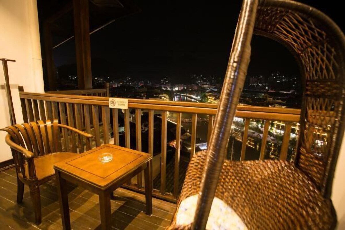 A balcony with a wooden table and chairs, a wicker chair, and a city view at night.