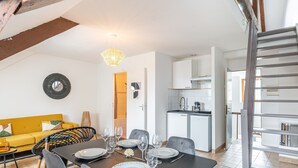 A dining area with a table set for four, a yellow sofa, and a kitchen in the background. - Le Guindy - Localisation idéale (Treguier)