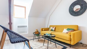 A cozy living room with a yellow sofa, a black chair, a small side table, and a round mirror on the wall. - Le Guindy - Localisation idéale (Treguier)