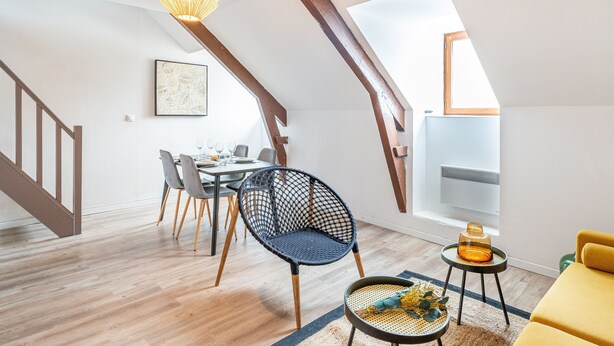 A modern loft apartment with a dining area, a black woven chair, a yellow sofa, and a wooden staircase. - Le Guindy - Localisation idéale (Treguier)