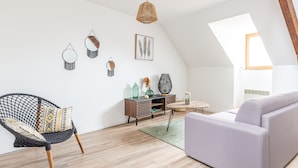A modern loft with a high ceiling, exposed wooden beams, a grey sofa, a woven chair, a wooden coffee table, and wall art. - Le Jaudy - Localisation idéale (Treguier)