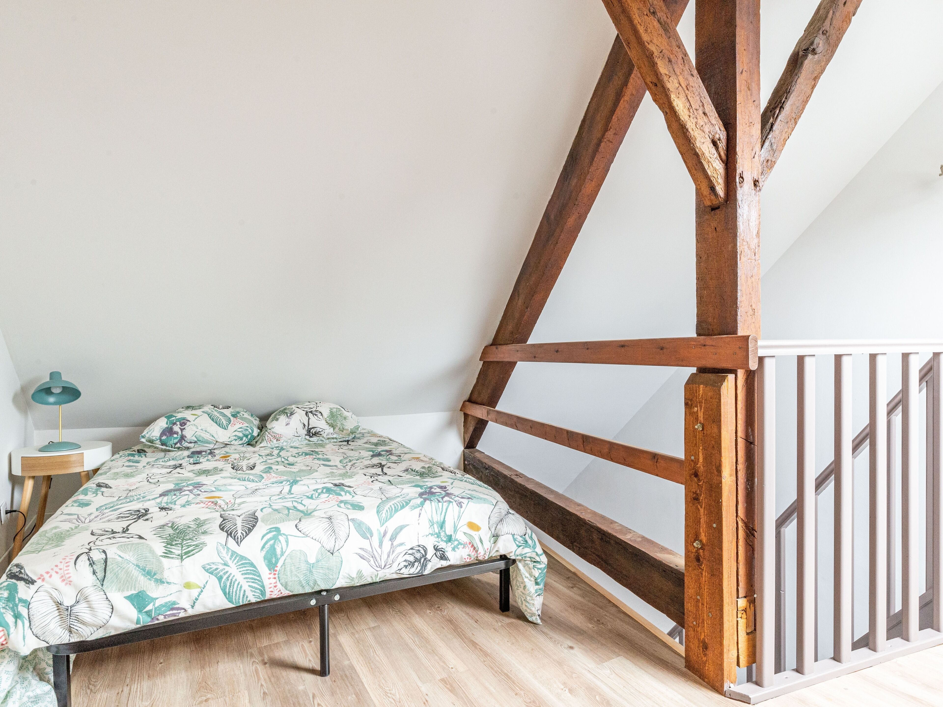 A bedroom with a bed, wooden beams, a nightstand, and a lamp.