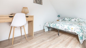 A bedroom with a wooden desk, white chair, and a bed with a floral bedspread. - Le Jaudy - Localisation idéale (Treguier)