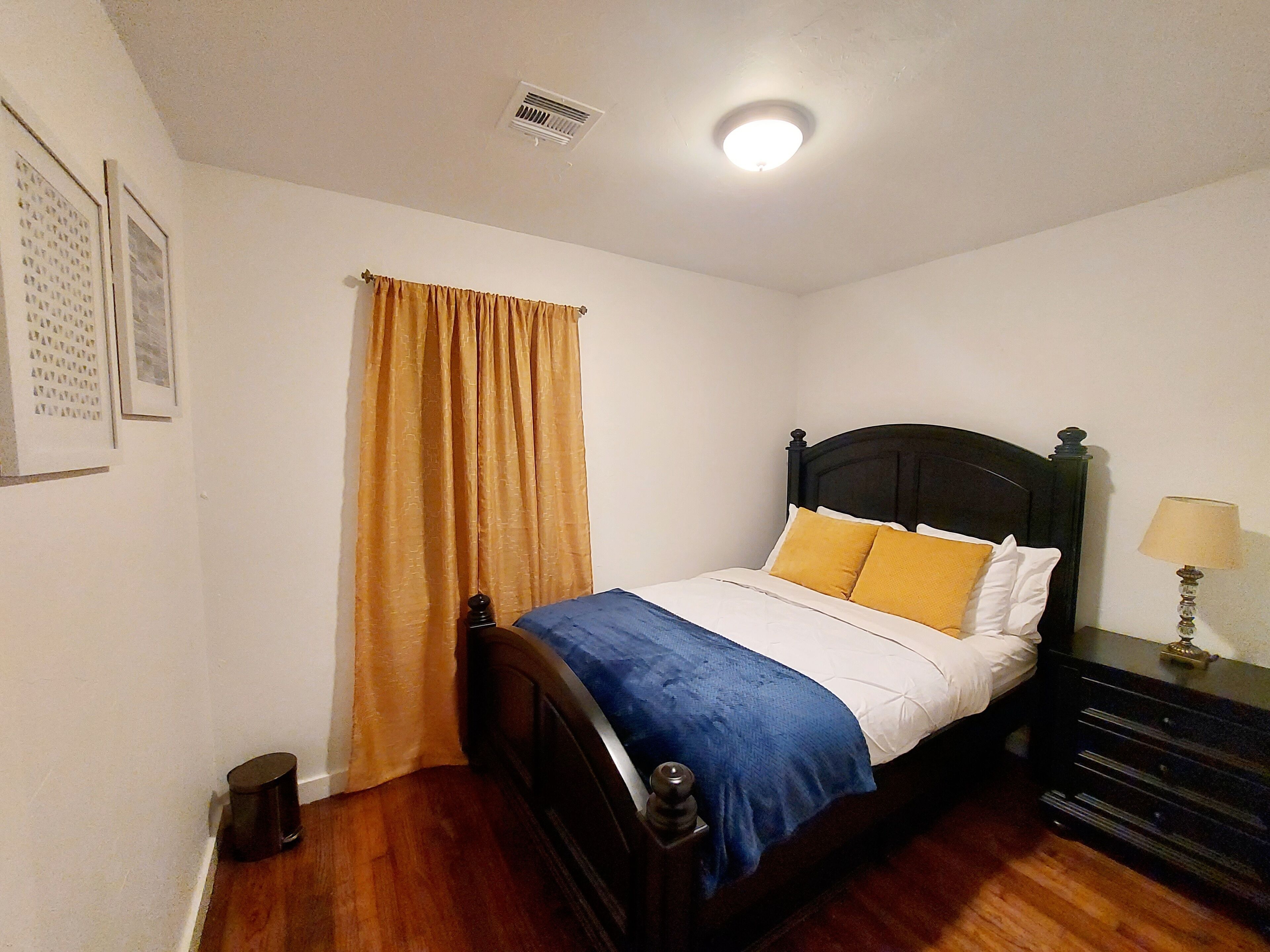 A bedroom with a single bed, a nightstand, a lamp, a window with curtains, and a ceiling light.