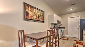 Un comedor con mesa y sillas de madera, una cocina con armarios y electrodomésticos blancos, y una puerta con marco blanco.