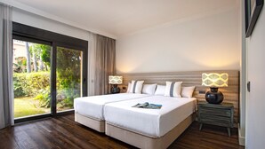 A double bed with a magazine, two bedside tables with lamps, a sliding glass door to a garden, and a wooden floor. - Genteel Home Venalmar Terrace (Estepona)