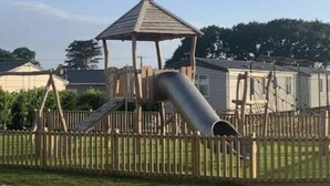 A playground with a wooden play structure, including a slide and a climbing area, surrounded by a wooden fence. - Serene Chalet Retreat (Southampton)