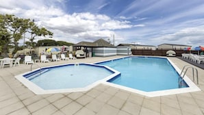 A swimming pool with two separate sections, surrounded by lounge chairs and umbrellas, under a clear sky. - Serene Chalet Retreat (Southampton)