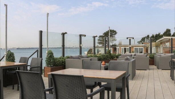 An outdoor patio with wicker furniture and a view of the water. - Serene Chalet Retreat (Southampton)