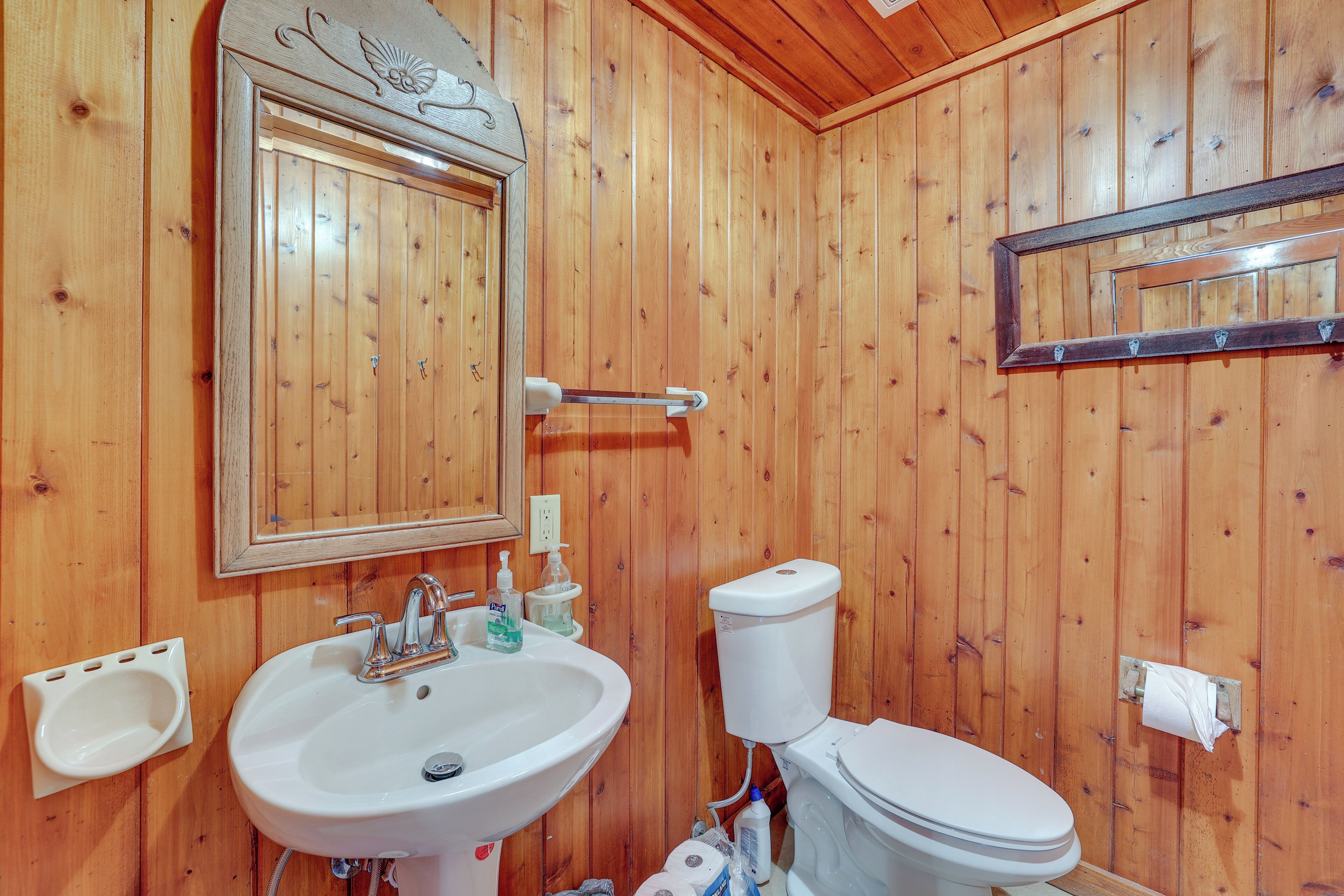 A wooden-paneled bathroom with a sink, mirror, toilet, and towel rack.