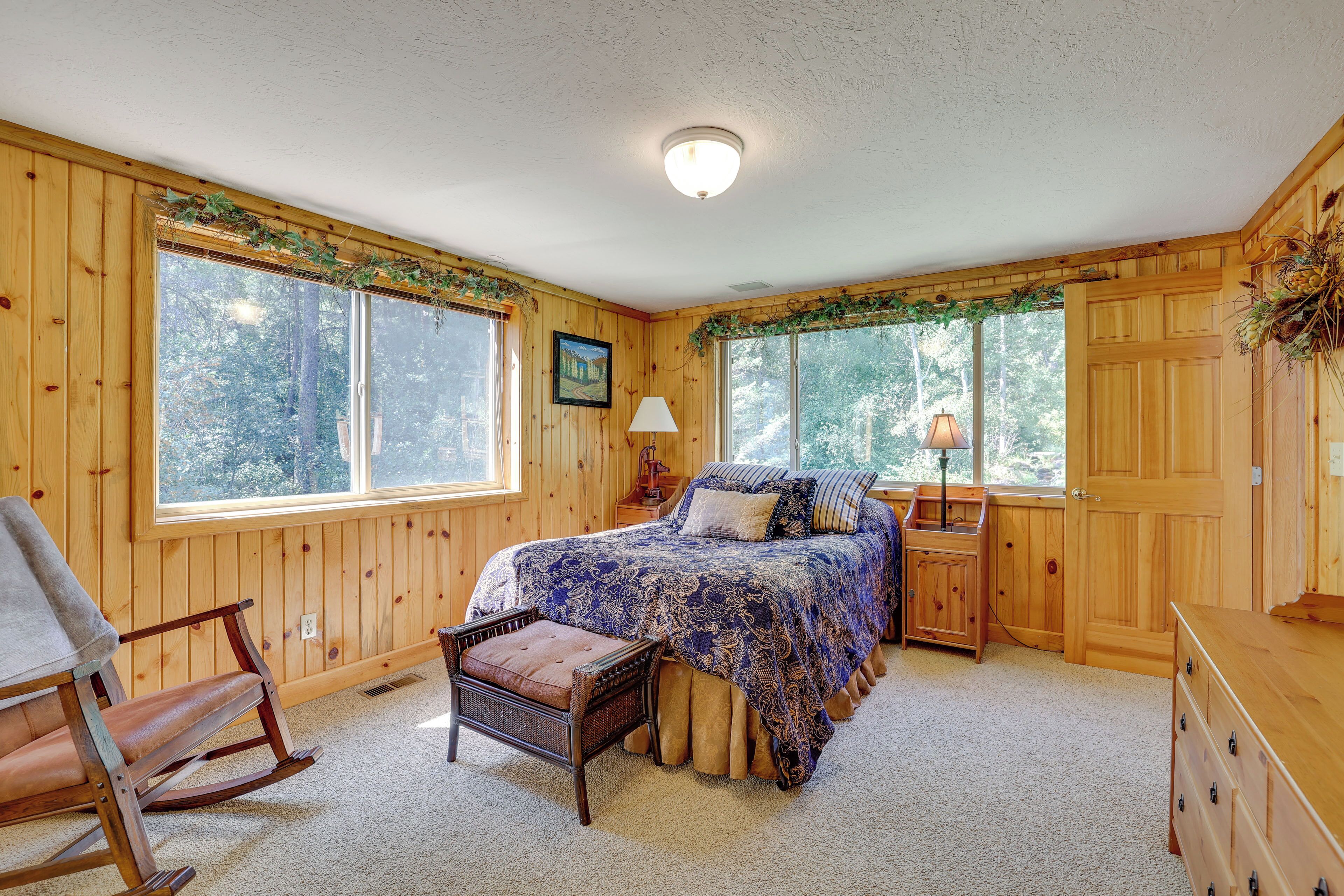 A cozy bedroom with a large bed, wooden walls, and a window overlooking a forest.