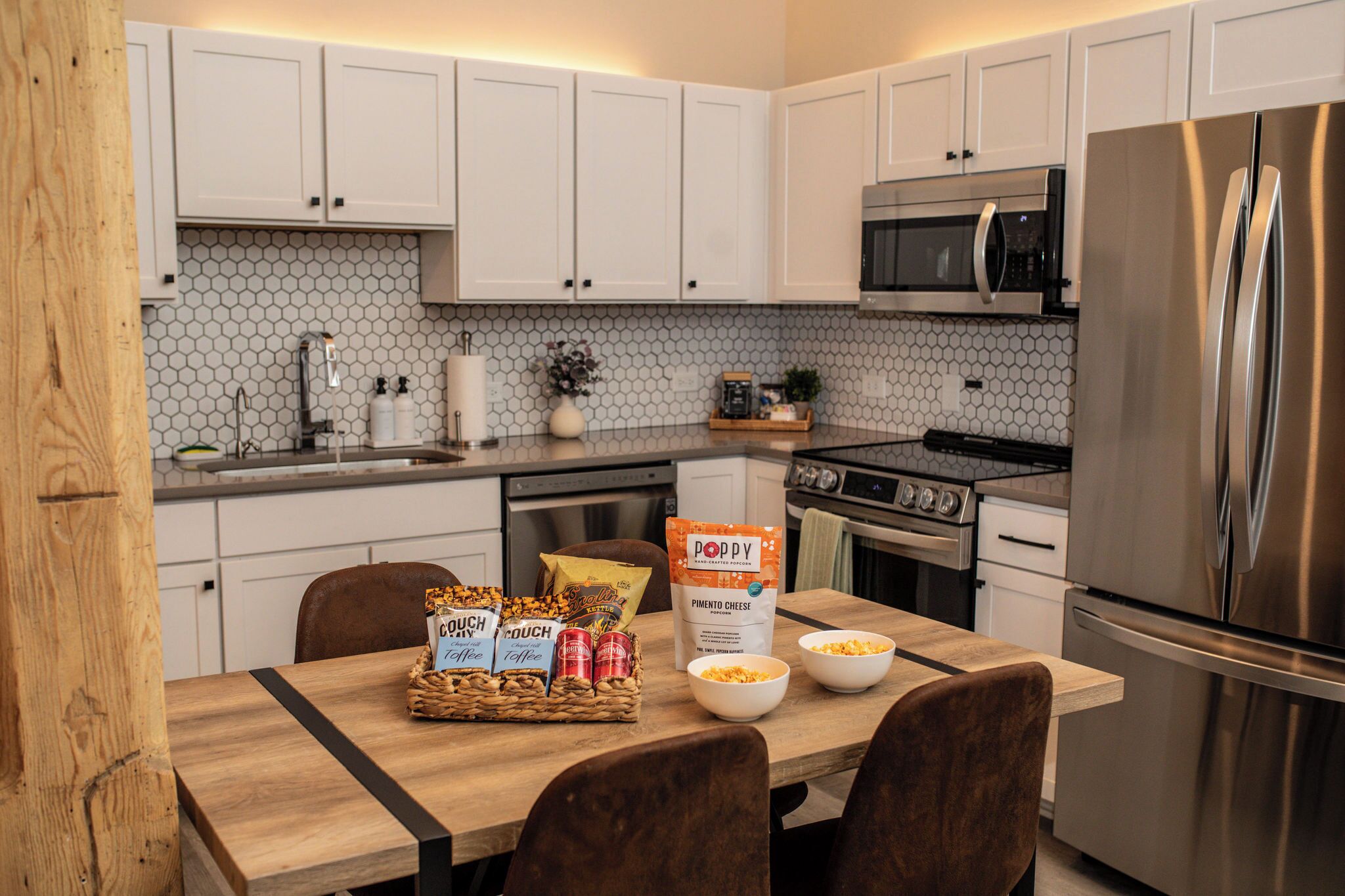 A modern kitchen with white cabinets, a stainless steel refrigerator, a microwave, and a wooden dining table with chairs.