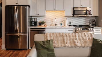 Cocina moderna con gabinetes blancos, electrodomésticos de acero inoxidable y encimera blanca.